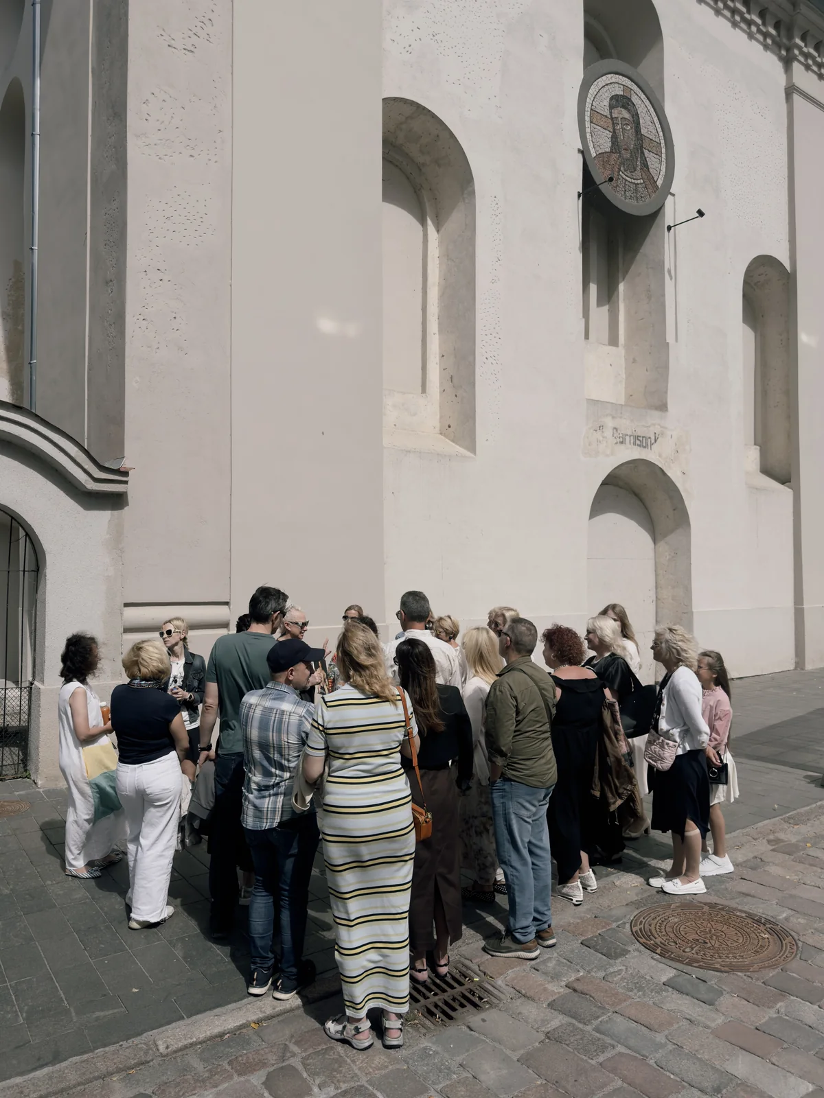 Tour group standing by the white wall of a church – “King Augustus' Letters” in Kaunas