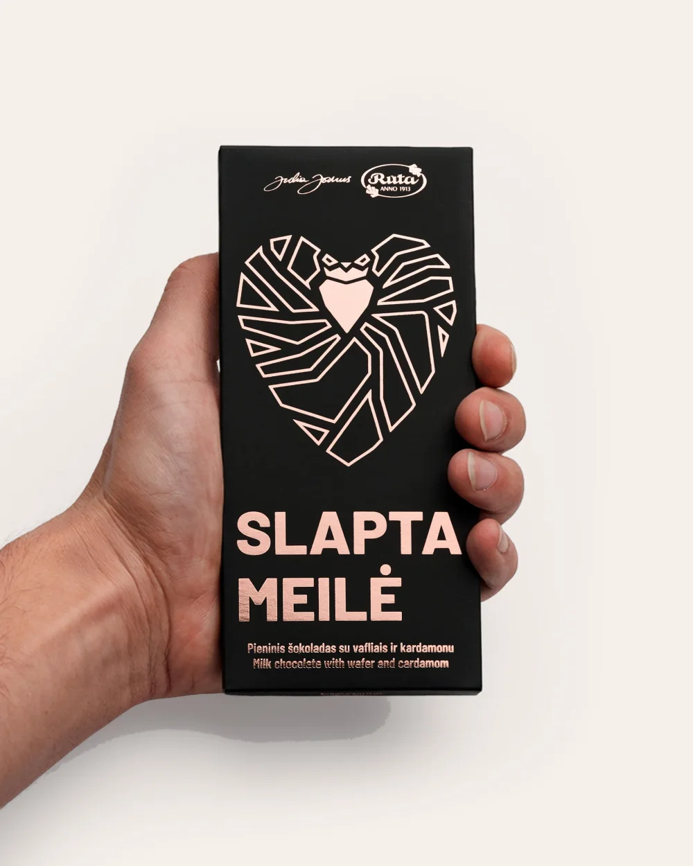 Black packaging of “Slapta meilė” milk chocolate with a pink heart, in a hand