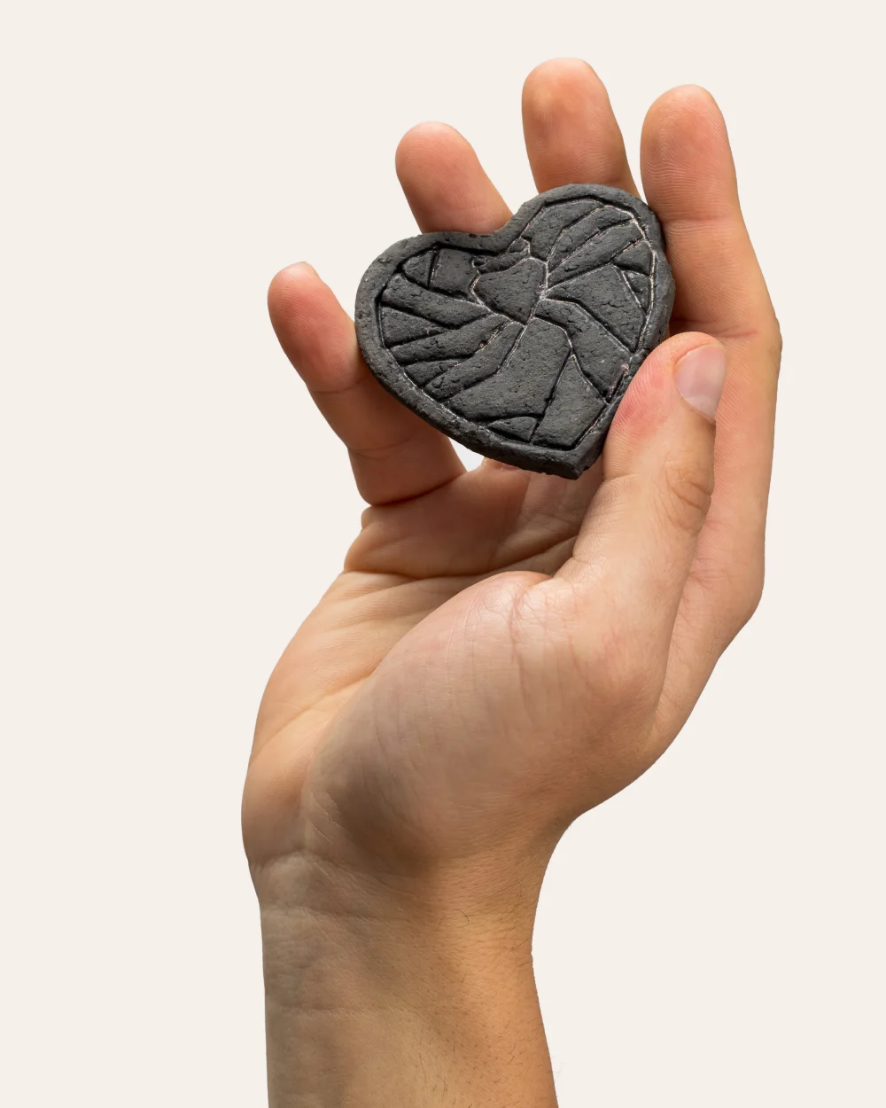 Tamsus reljefinis magnetukas „Karūnuota širdis širdyje“ laikomas pakeltoje rankoje