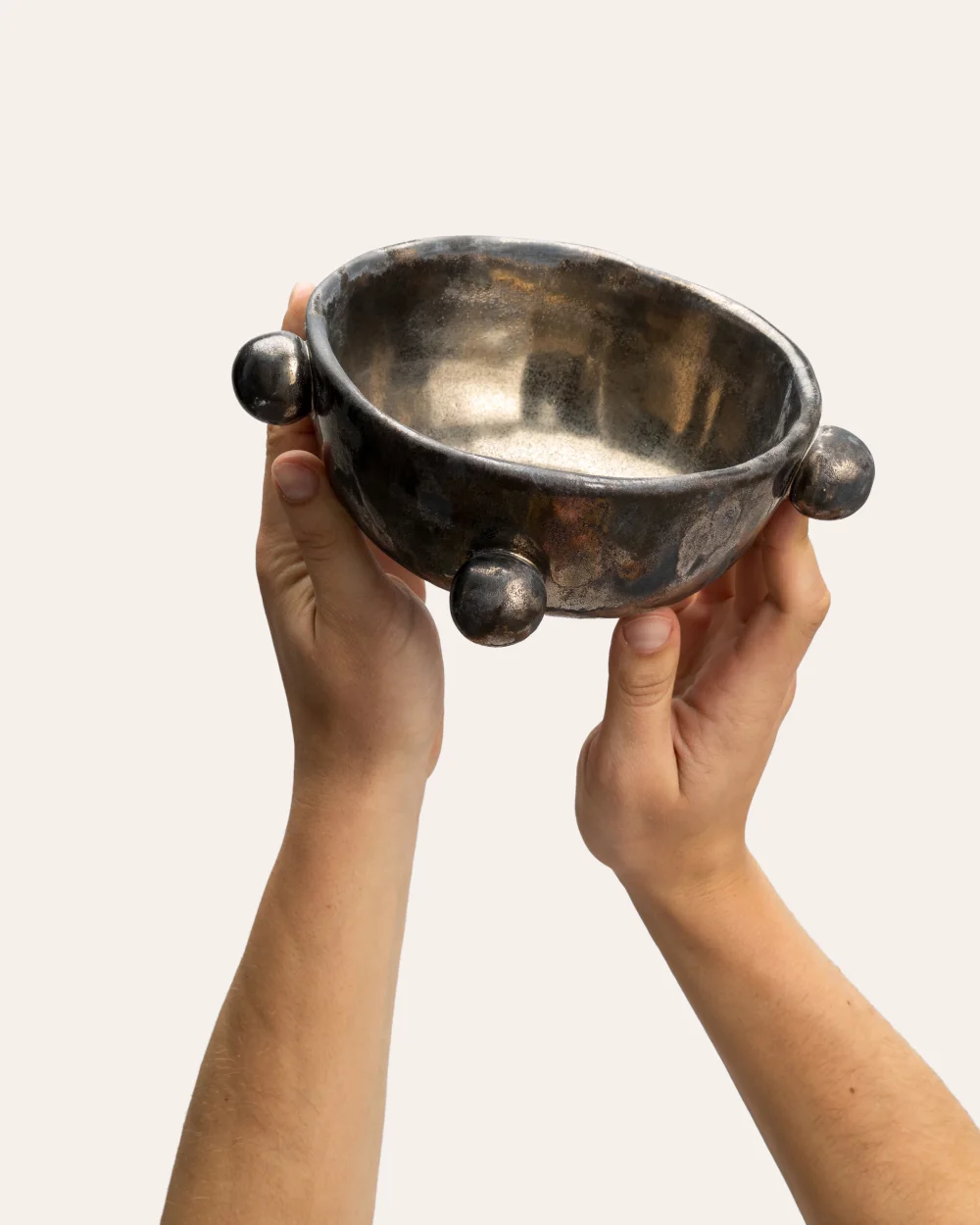 Small dark gold “The Queen's Pearl Bowl” raised in two hands, showing the inside