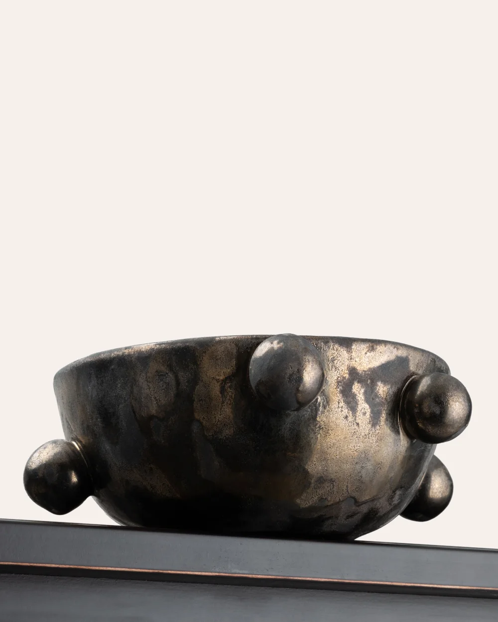Side of the small dark gold “The Queen's Pearl Bowl” with balls on a shelf