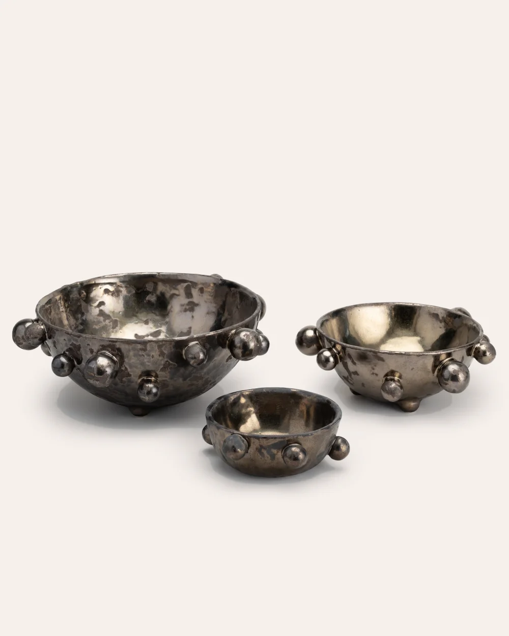 Three dark gold “The Queen's Pearl Bowl” bowls in different sizes on a light background