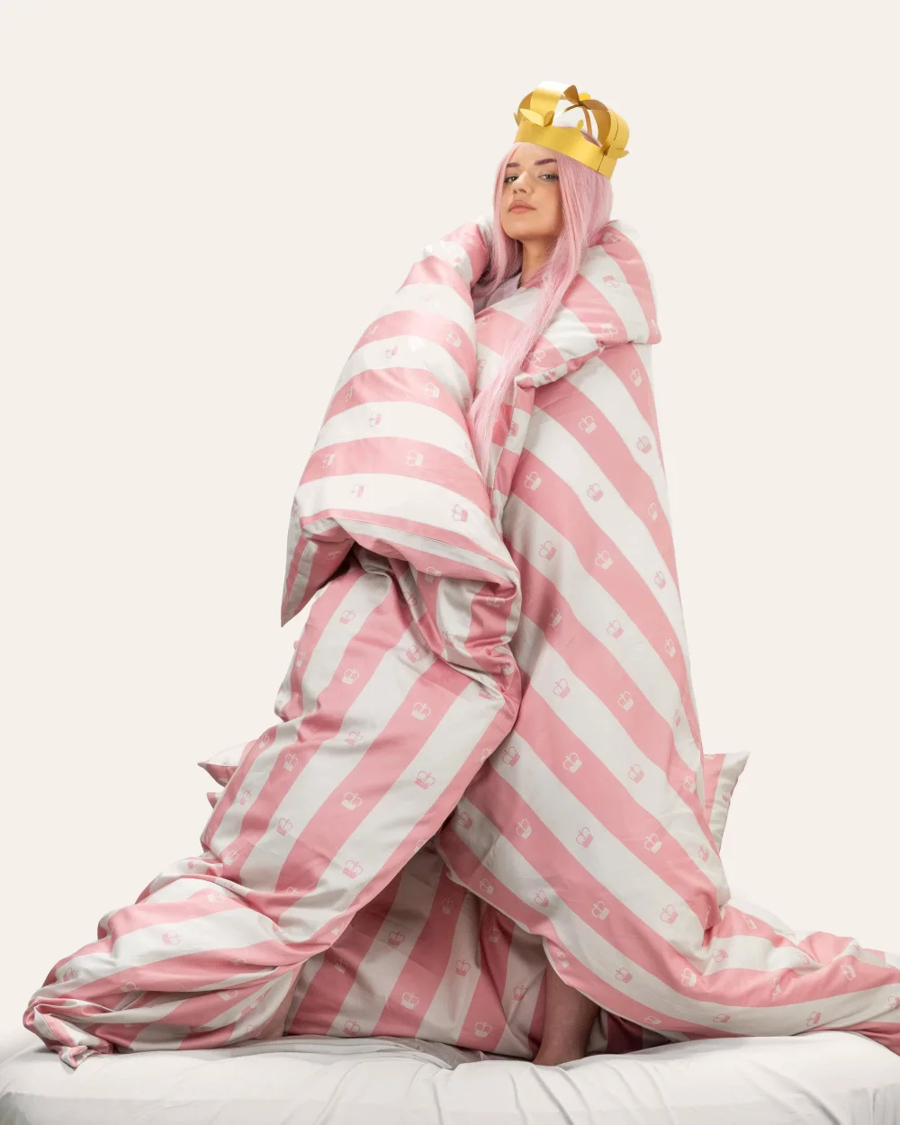 Girl with a crown standing wrapped in a pink striped “Your Majesty” duvet
