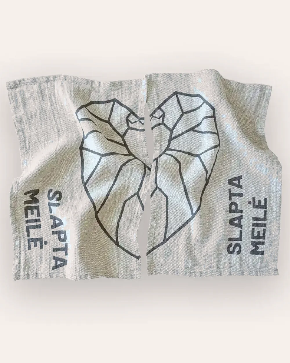 Grey “Slapta meilė” linen face towel with a graphite heart drawing, laid flat