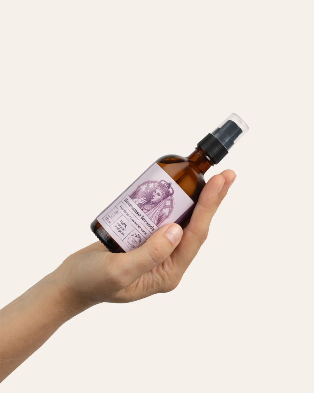 A brown glass spray bottle of “Renaissance Lavender” lavender hydrosol held diagonally in a hand