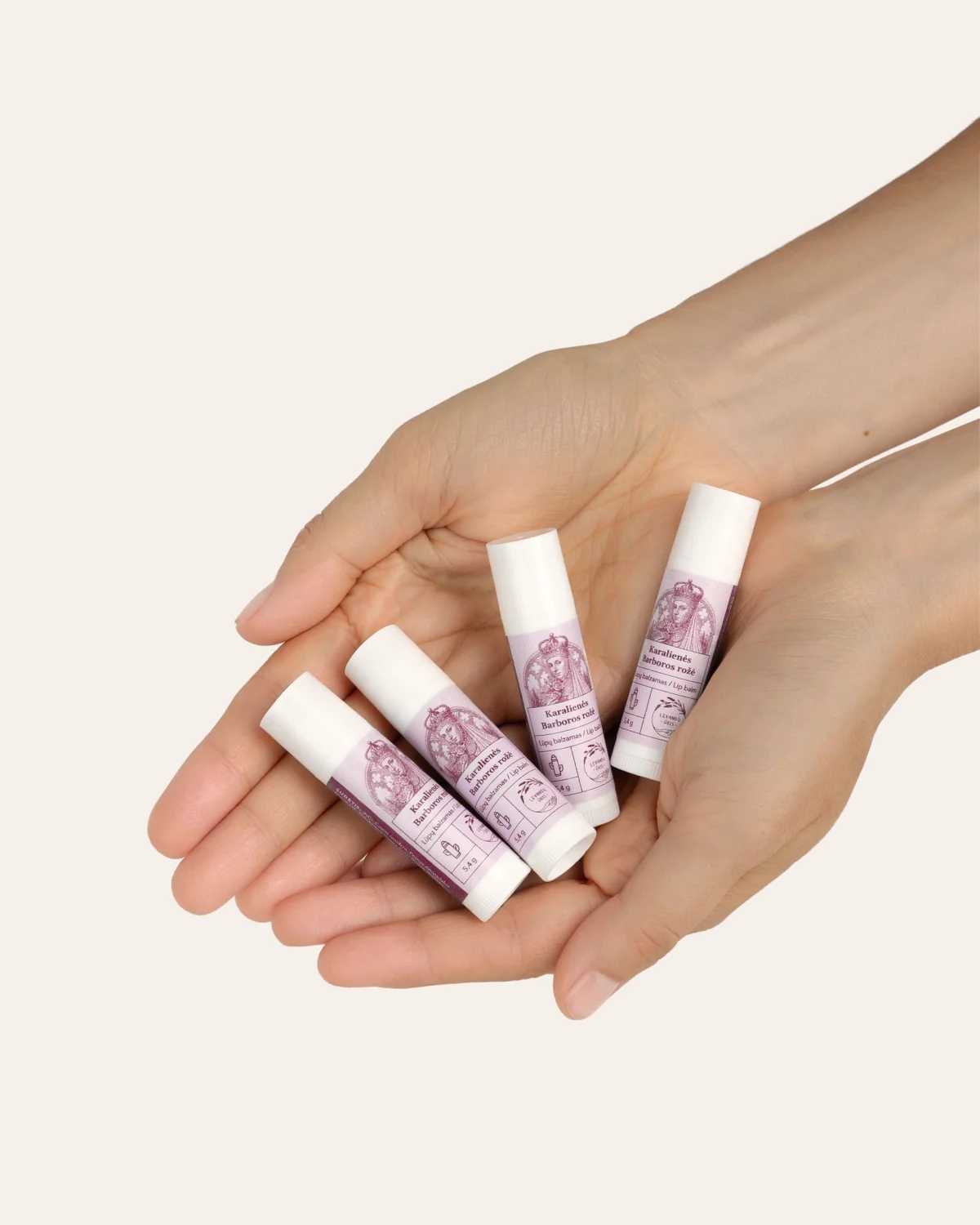 Four “Queen Barbara's Rose” lip balms placed in cupped hands