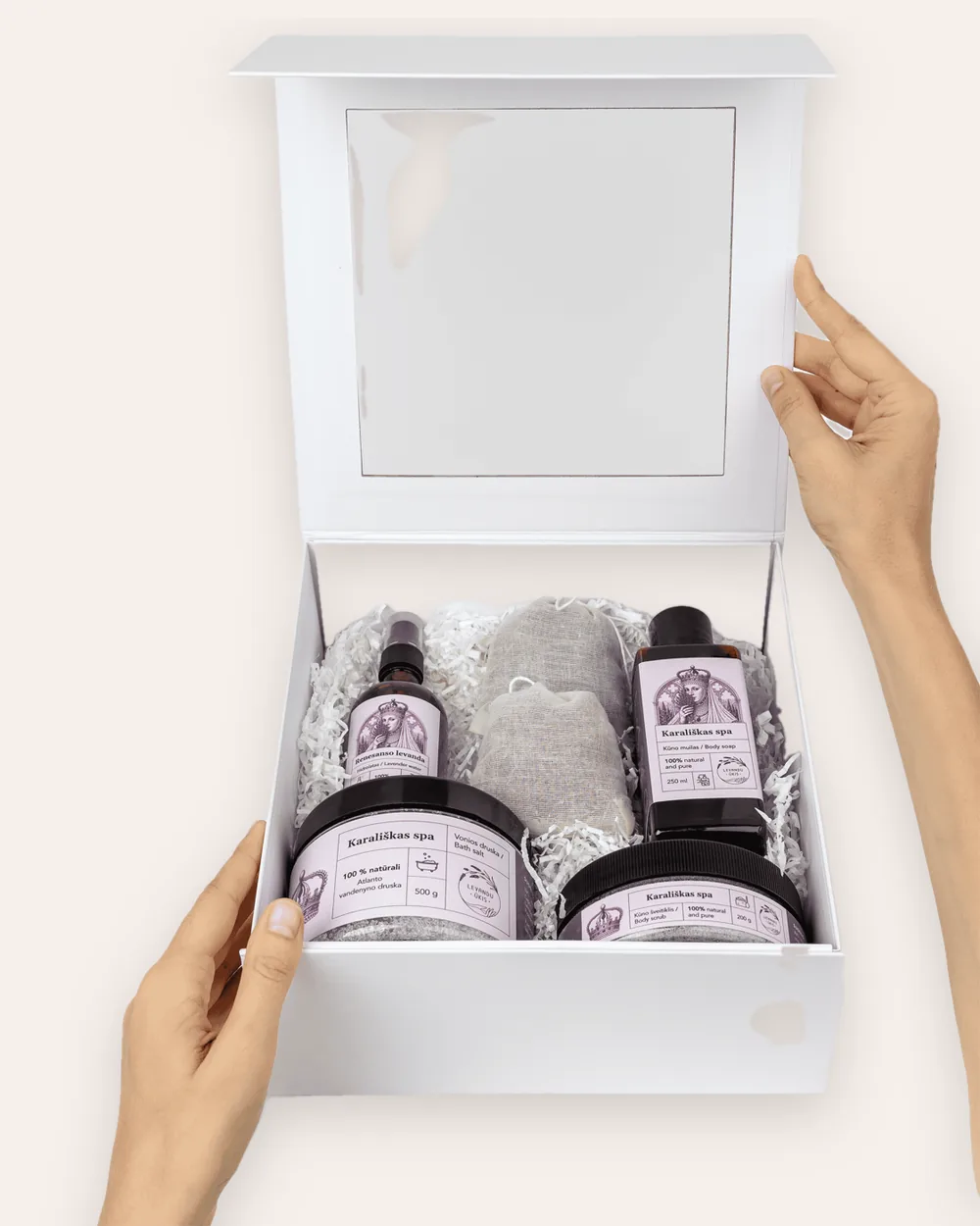 Atidaryta balta dovanų dėžė „Karališkas SPA“ su levandų produktais, laikoma rankomis