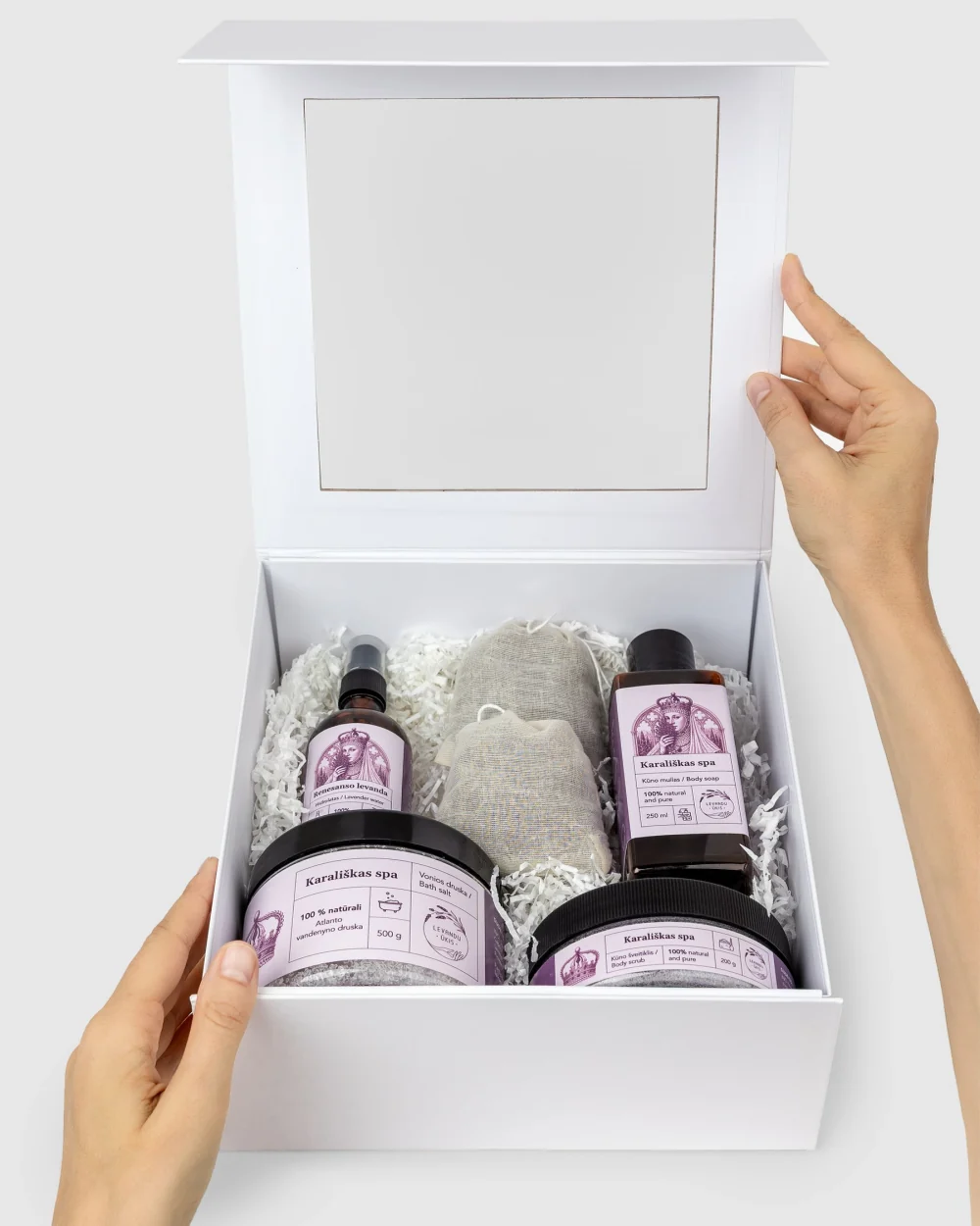 Atidaryta balta dovanų dėžė „Karališkas SPA“ su levandų produktais, laikoma rankomis