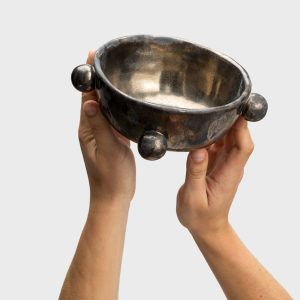 Small dark gold “The Queen's Pearl Bowl” raised in two hands, showing the inside