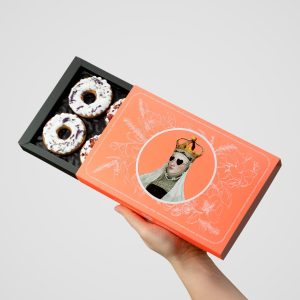 Hand holding an open orange box of “Queen Barbara's” gingerbread with iced flowers
