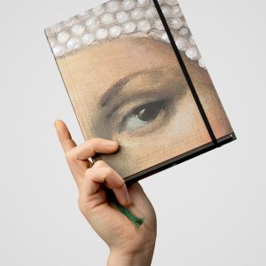 “Slapta meilė | Barbara Radziwiłł” notebook with a woman's eye detail on the cover, raised in a hand