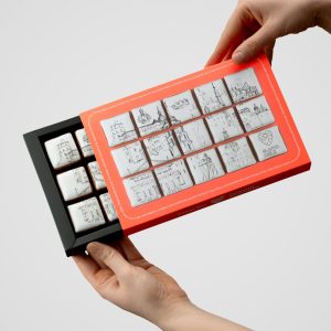 Hands opening a box of square “Royal Vilnius” gingerbread biscuits with drawings of Vilnius