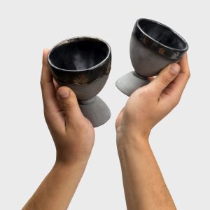 Two black ceramic “Kings' Goblets” with metallic rims in two hands