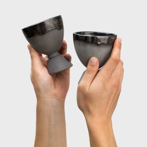Two black ceramic “Kings' Goblets” held in hands, side view