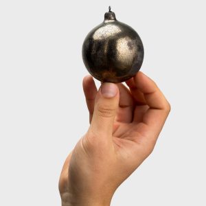 Dark gold “Pearl of the Vilnius Crown” Christmas bauble held in a hand on a light background