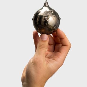 Dark gold “Royal Pearl” Christmas ornament with pearl details in a hand on a light background