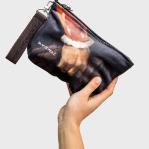 “Augustus” cosmetic bag with a dark handle and a painted hand image, held in a raised hand