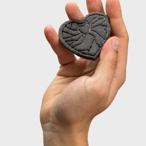 Dark relief “Crowned Heart Within a Heart” magnet held in a raised hand