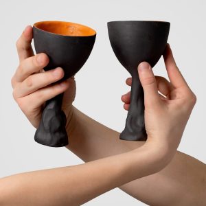 Two crossed hands hold two black Kings' Goblets with orange insides