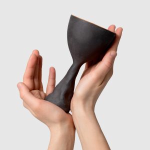 Two hands hold a black Kings' Goblet with a sculpted stem, angled view