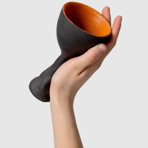 Hand holding a tilted black Kings' goblet, showing the orange glaze inside