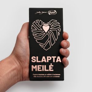 Black packaging of “Slapta meilė” milk chocolate with a pink heart, in a hand
