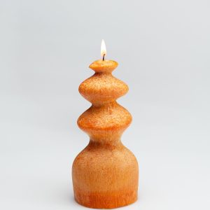 Orange wave-shaped candle “Queen Barbara” burning on a light background