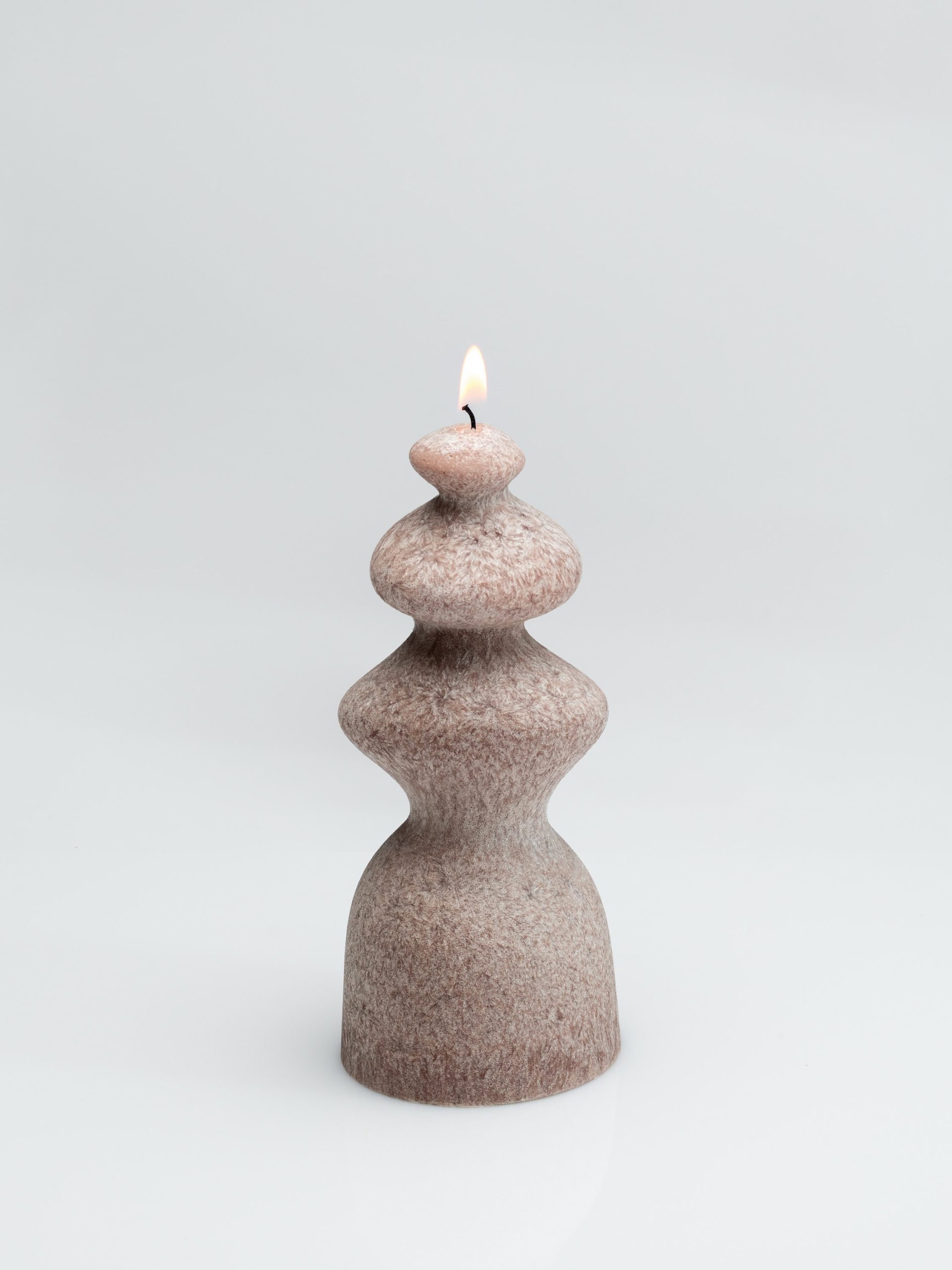 Powder-coloured wave-shaped “Queen Barbara” candle burning on a light background