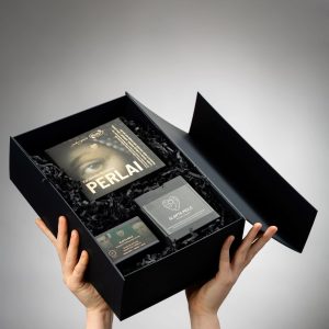 Hands holding an open black “Tales of the Royal Court” gift box with chocolate and a book