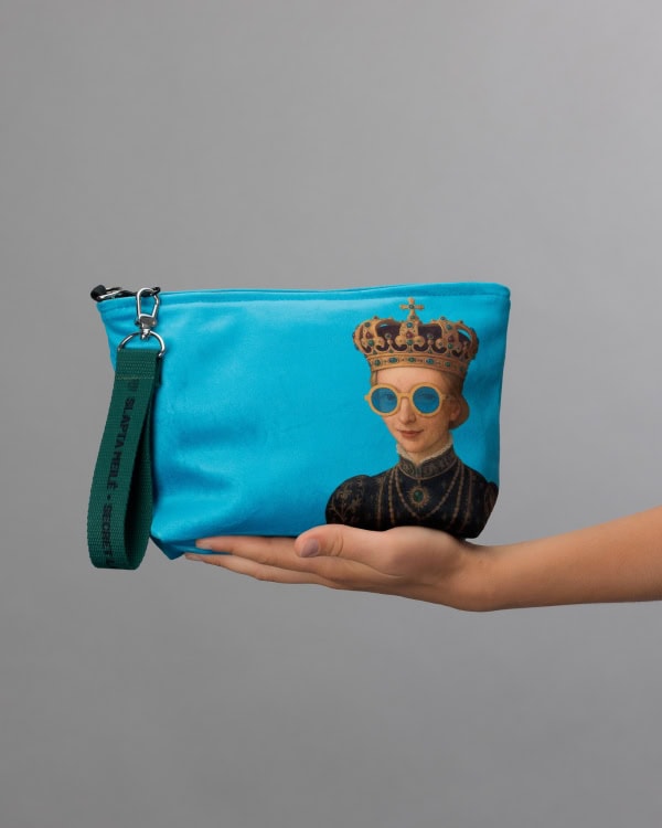 Niebieska kosmetyczka „IMMIGRANT QUEEN: Sweden Edition” z rysunkiem koronowanej kobiety w okularach na dłoni