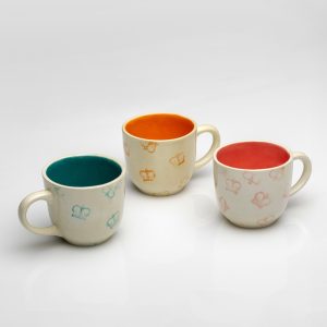 Three “Very Royal” mugs with green, orange and red insides on a light background
