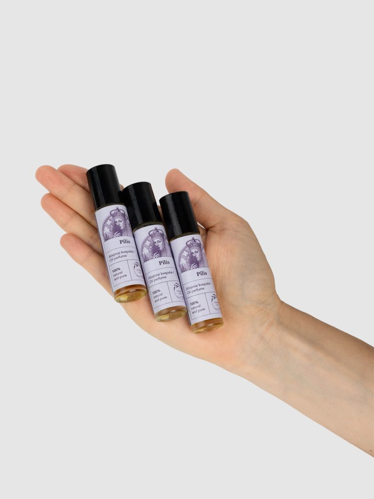 Hand holding three bottles of “The Castle” oil perfume with purple labels