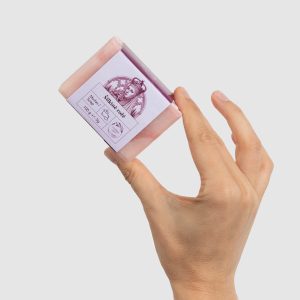 Hand holding a pink 100 g bar of “Silky Rose” soap with a label, angled view