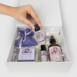 Hand placing a bottle into the “Queen Barbara's SPA” set with a lavender sachet in a white box