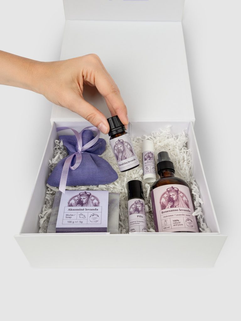Hand placing a bottle into the “Queen Barbara's SPA” set with a lavender sachet in a white box