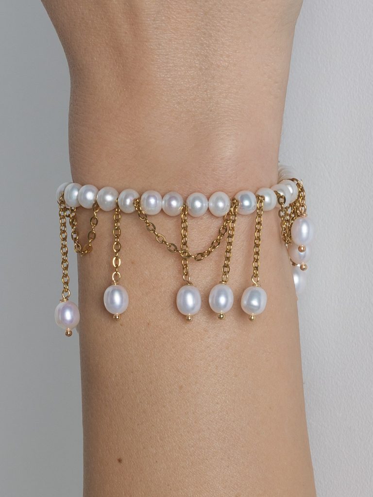 Gold-coloured pearl bracelet “The Queen's Whim” with dangling chains on a wrist