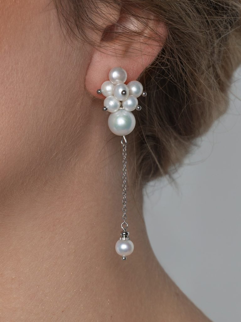 Close-up of the earring “The Queen's Garden” with a cluster of pearls and a hanging pearl on a model's ear