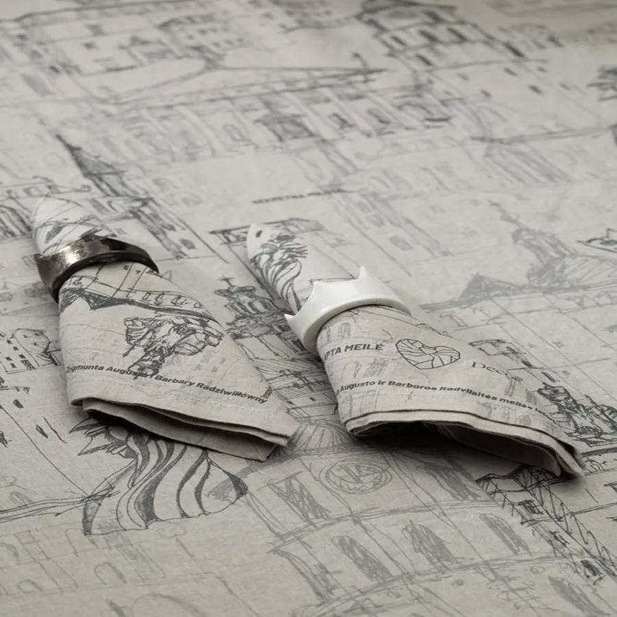 Two folded “Royal Vilnius Love Story” linen napkins with rings on a tablecloth