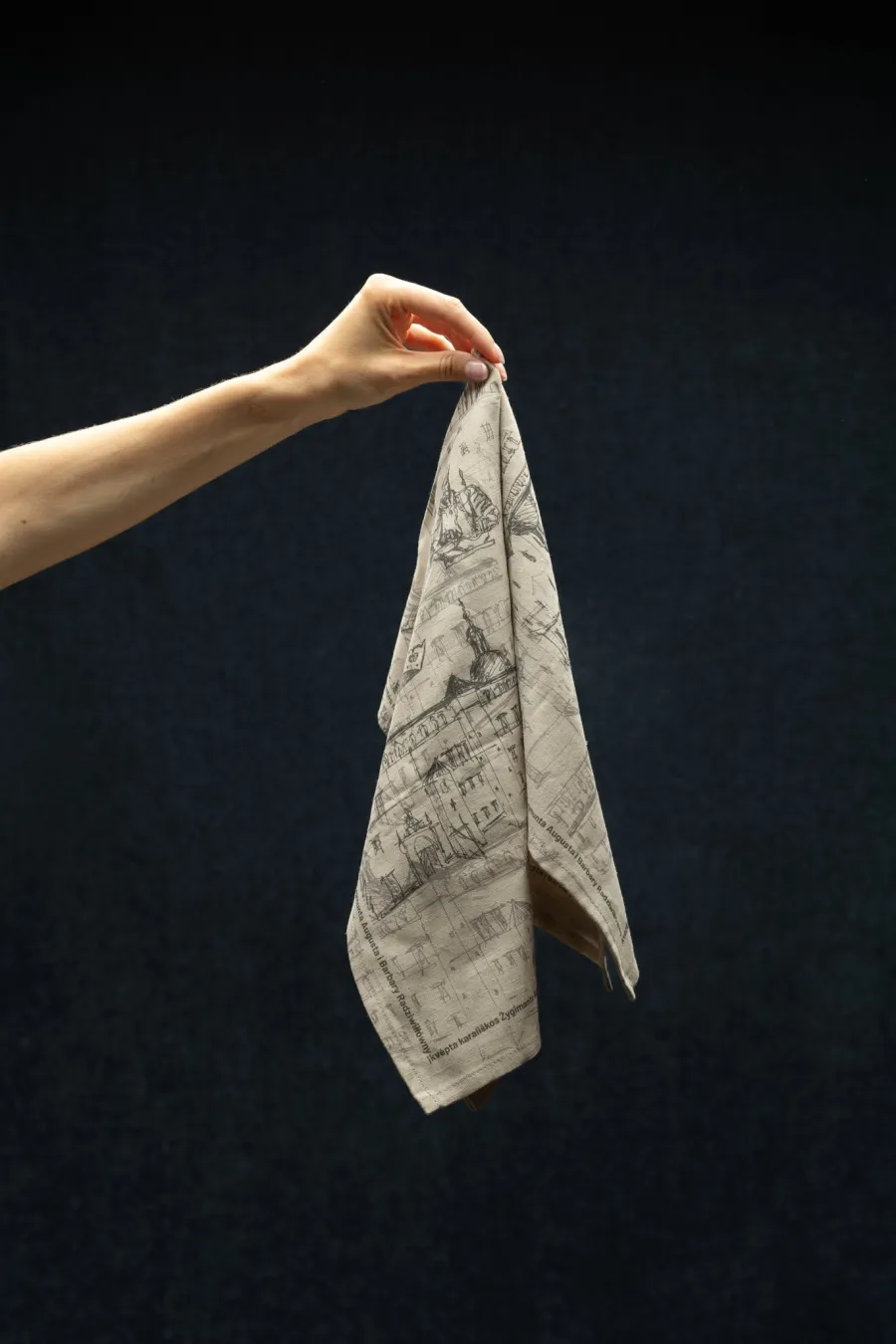Hand holding a “Royal Vilnius Love Story” linen napkin on a dark background
