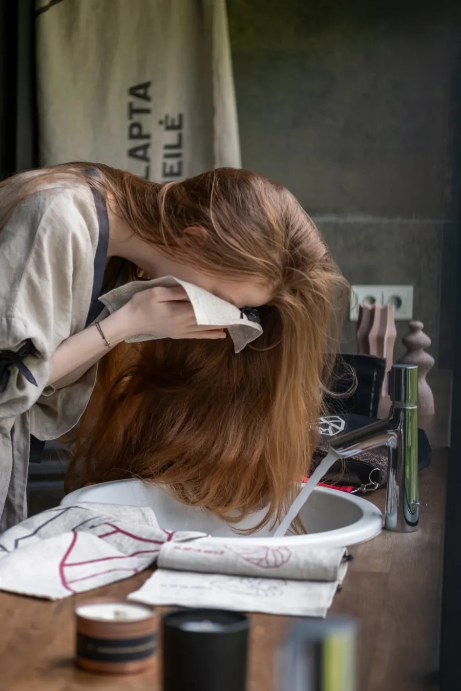 Woman drying her face with a “Slapta meilė” linen face towel by a washbasin
