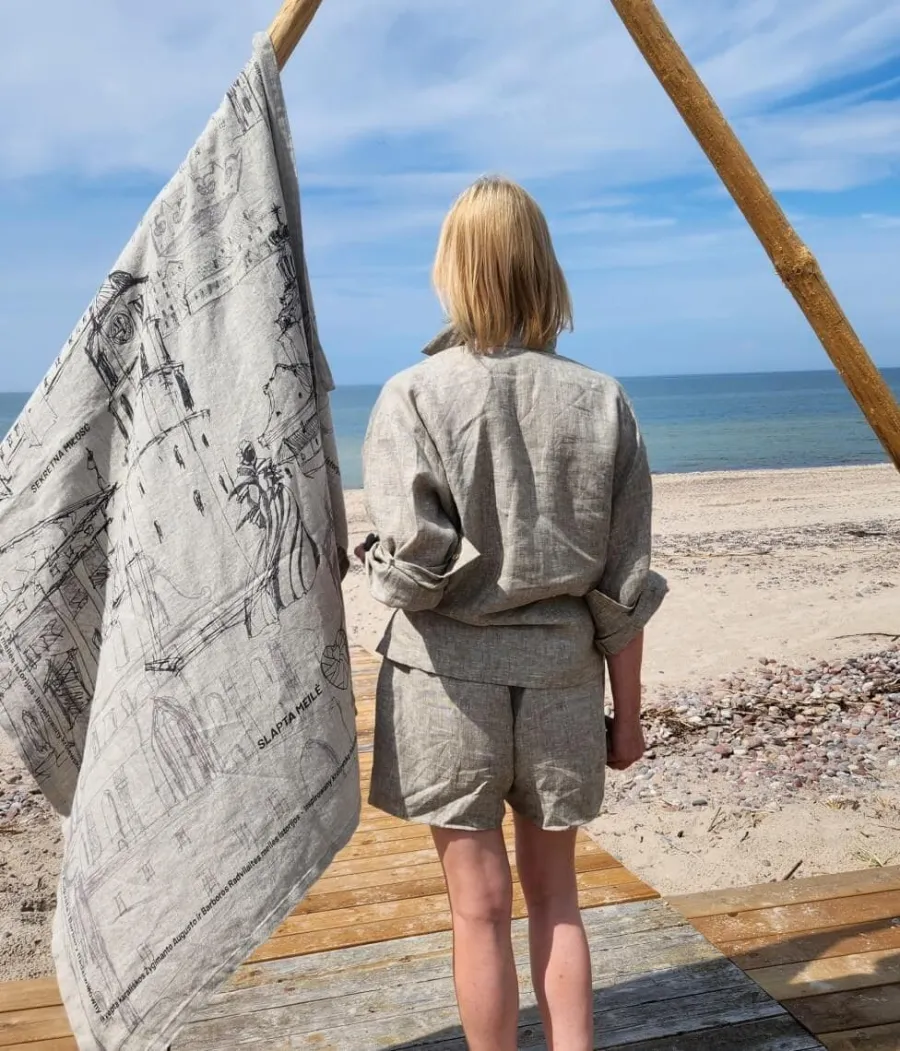 Woman on a beach next to a “Royal Vilnius Love Story” towel hanging on a rail