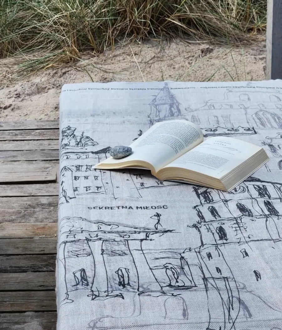 “Royal Vilnius Love Story” linen towel with a Vilnius drawing and a book on a terrace