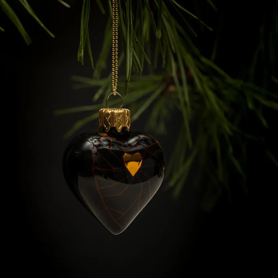 Black heart-shaped “Crowned Heart” Christmas ornament with a small gold crown on a pine branch