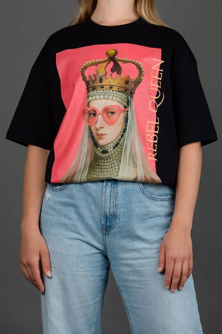 Woman in a black “REBEL QUEEN” T-shirt and light jeans, hand in pocket