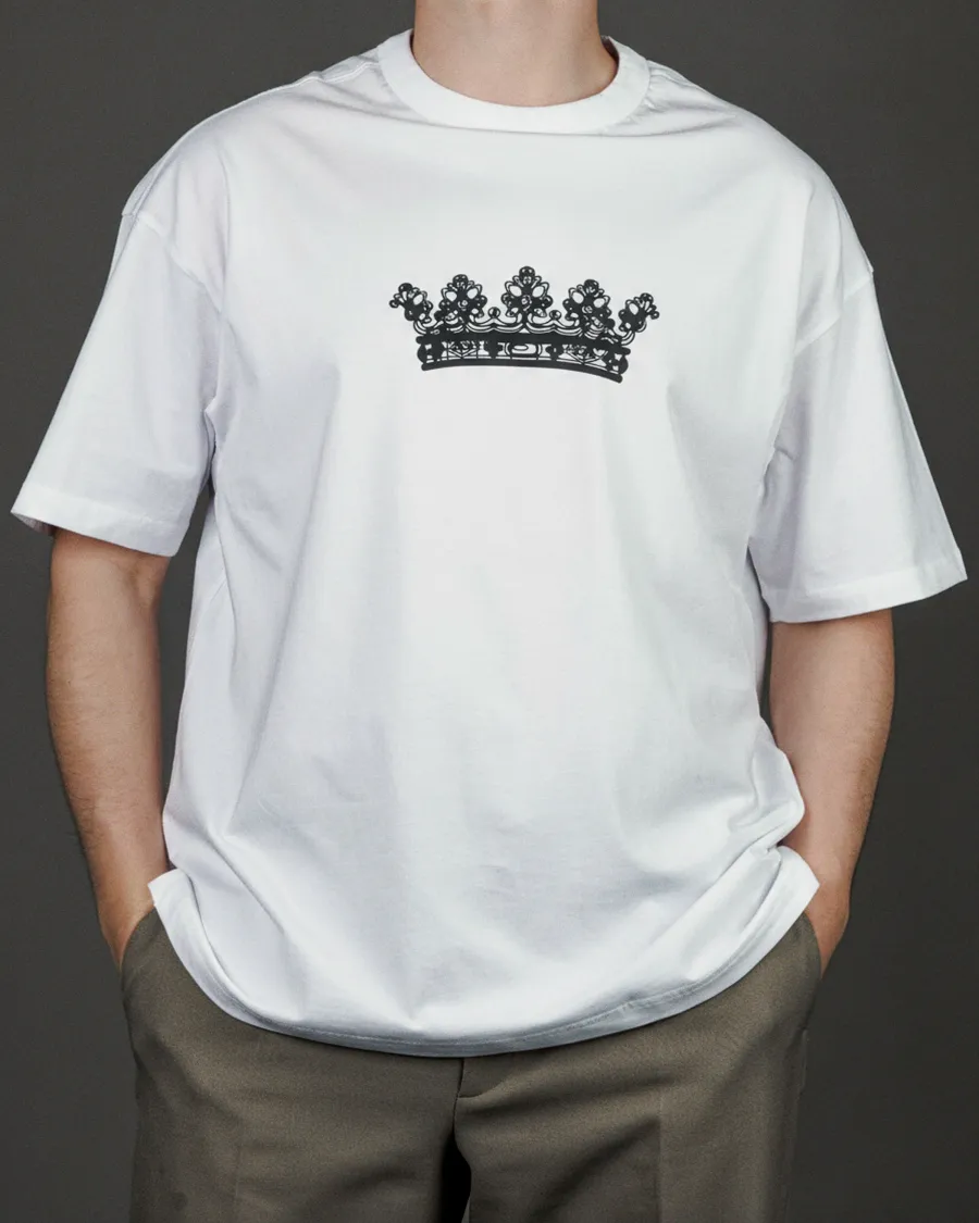Man wearing a white “KARŪNA” T-shirt with a black crown drawing on the chest