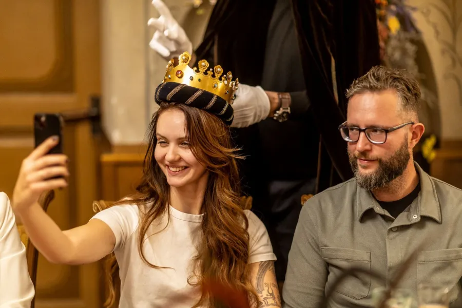 A woman is crowned with a golden crown and takes a photo with her phone – Vilnius Royal Hunt Dinner