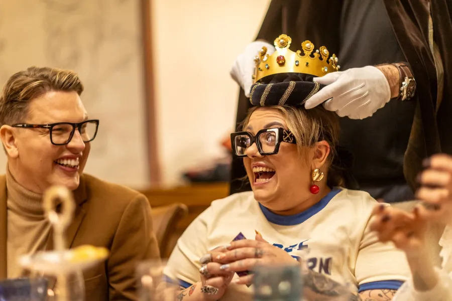 A crown being placed on a laughing woman in glasses – Vilnius Royal Hunt Dinner
