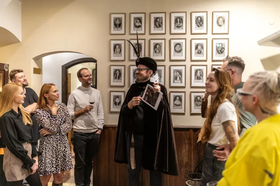 Host in a cloak and guests by a wall with paintings – Vilnius Royal Hunt Dinner