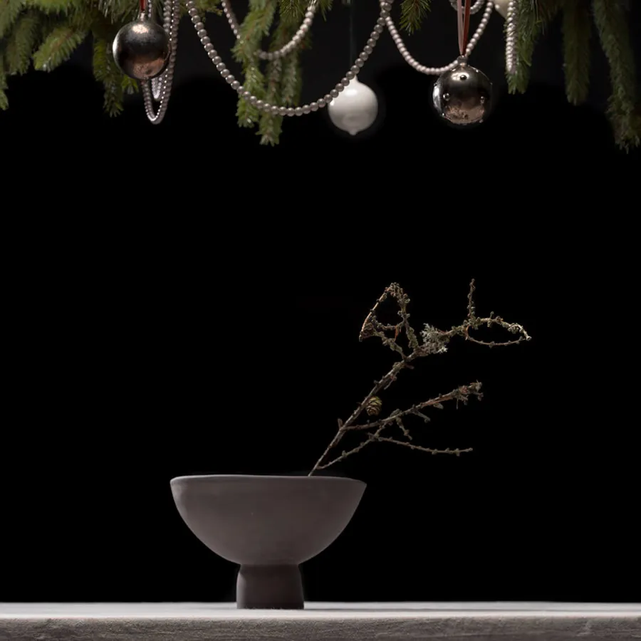 Dark Renaissance-style bouquet vase with a dry twig on a black background beneath Christmas ornaments