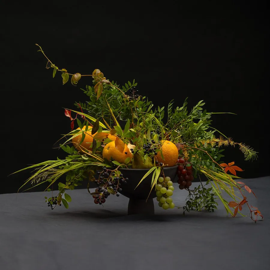 Renaissance-style bouquet vase with oranges, grapes and greenery against a dark background
